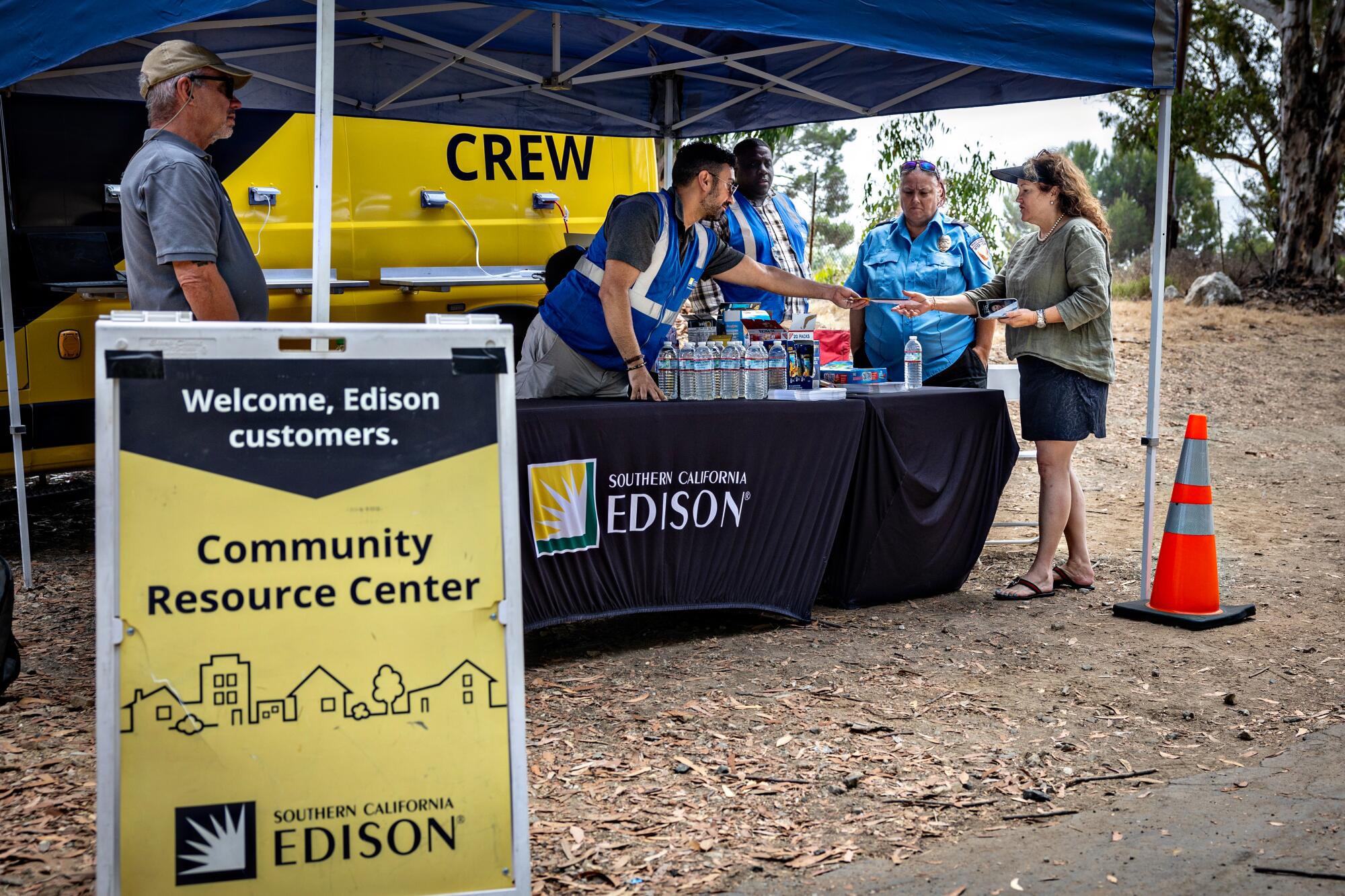 People behind tables under a tent speak to other people.