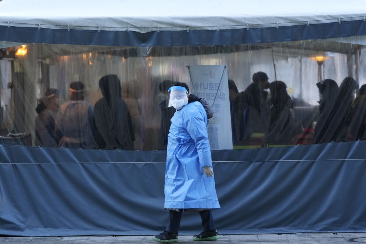 A medical worker passes by people as they wait for their coronavirus tests at a makeshift testing site in Seoul, South Korea, Thursday, Feb. 3, 2022. (AP Photo/Ahn Young-joon)
