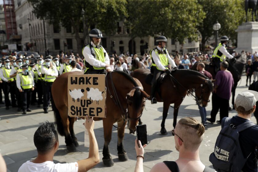 A protester holds up a placard in front of police officers during a "Resist and Act for Freedom" protest against a mandatory coronavirus vaccine, wearing masks, social distancing and a second lockdown, in Trafalgar Square, London, Saturday, Sept. 19, 2020. (AP Photo/Matt Dunham)
