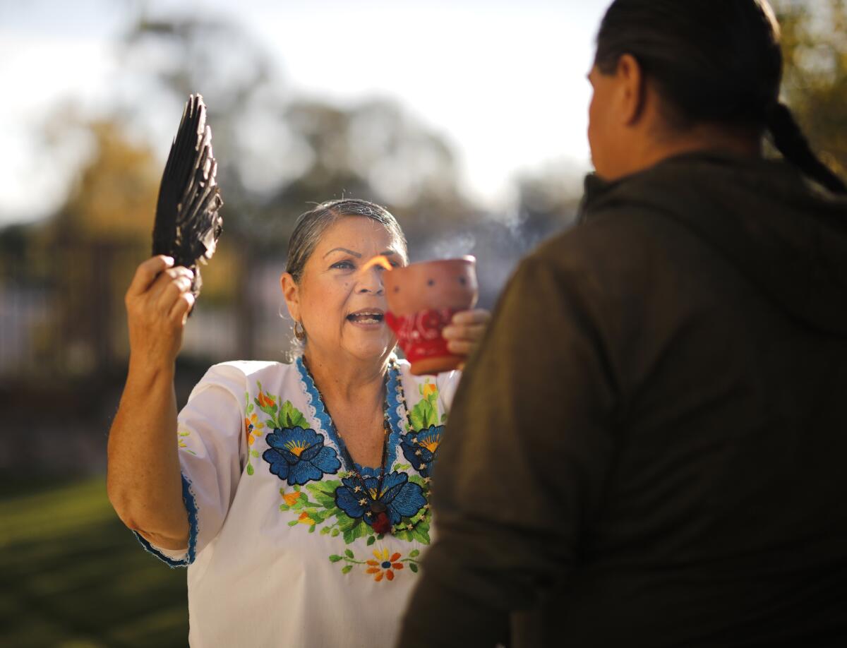 A woman holds up a wing and a candle in front of a client during a spiritual cleansing.