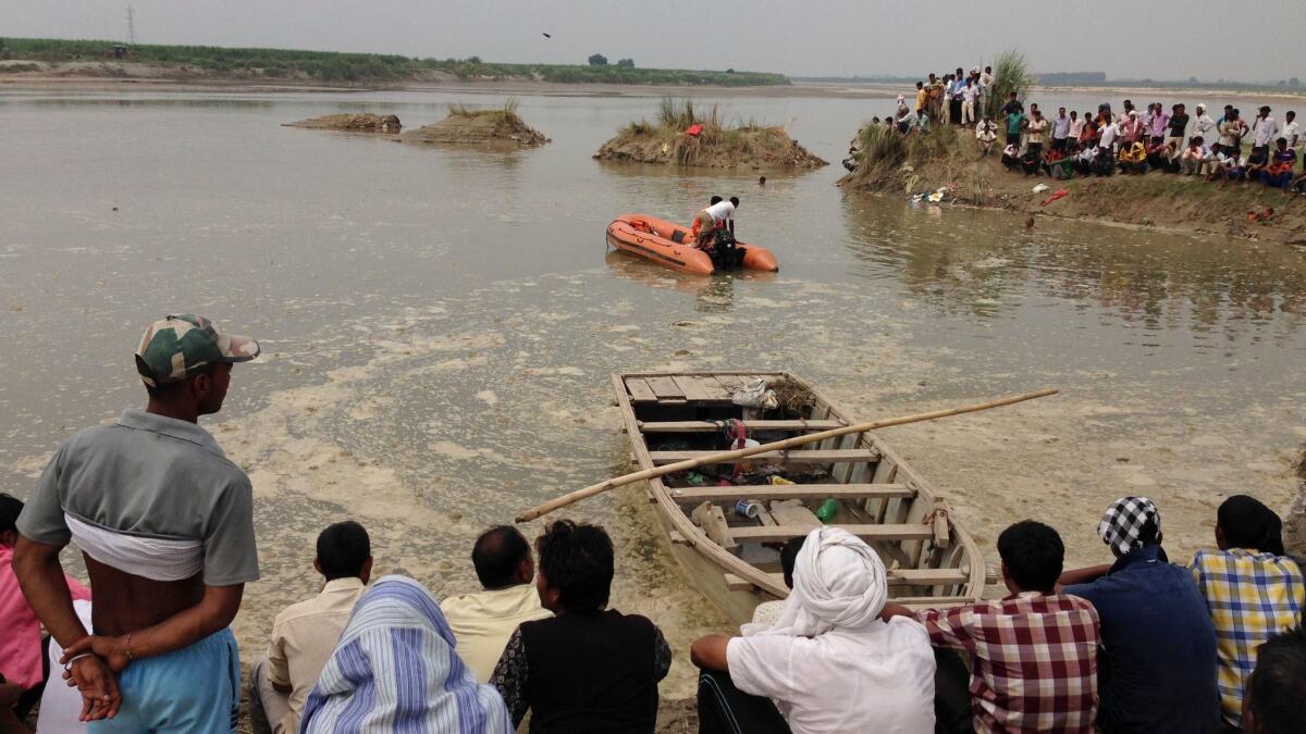 Villagers watch as rescuers search the Yamuna River after a boat, seen in foreground, capsized in Uttar Pradesh state.