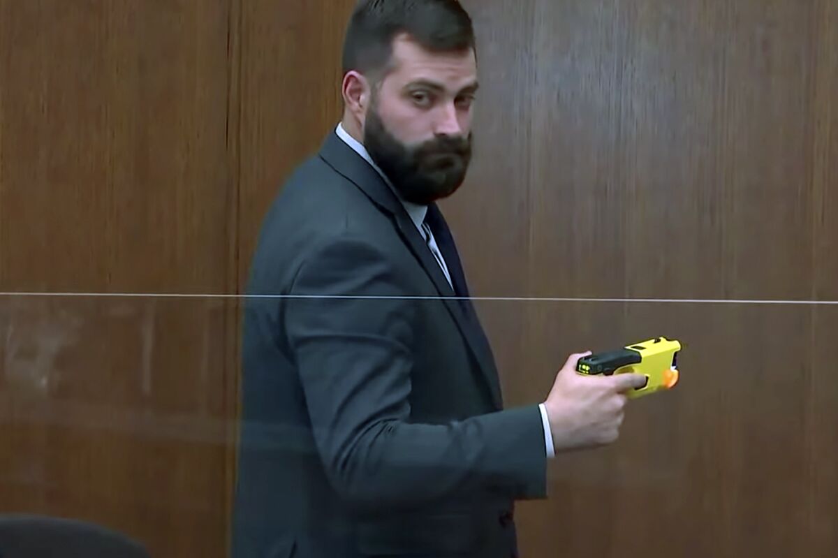 Sam McGinnis, senior special agent with the Minnesota Bureau of Criminal Apprehension, holds the taser of Brooklyn Center police Officer Kim Potter as he testifies while Hennepin County Judge Regina Chu presides over court Monday, Dec. 13, 2021, in the trial of Potter in the April 11, 2021, death of Daunte Wright, at the Hennepin County Courthouse in Minneapolis. (Court TV via AP, Pool)