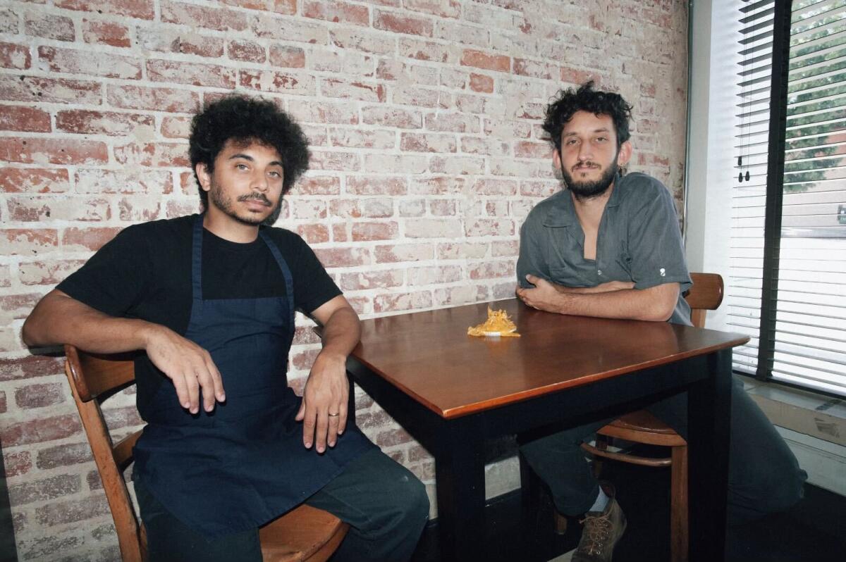 Miles Thompson, left, and beverage director Andy Schwartz sit at a table in Baby Bistro in Koreatown against a brick wall