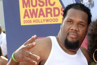 FatMan Scoop in a white tank top holding up a peace sign as he poses against at a red carpet event