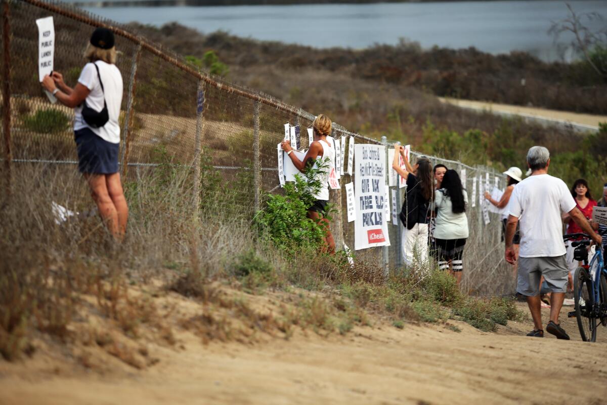 Protesters put signs on the fence demonstrating against the proposed and failed sale of the property to a political donor.