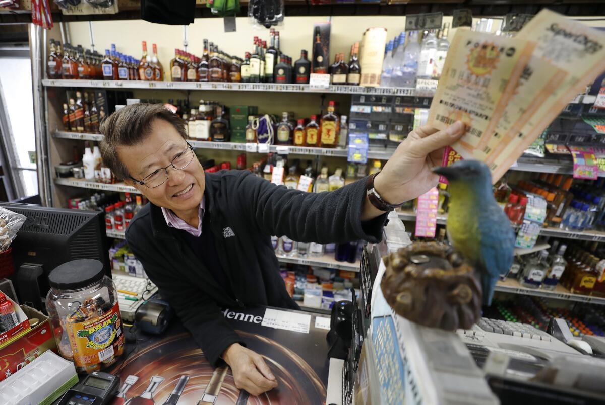 James Kim, owner of Bluebird Liquor in Hawthorne rubs lottery tickets purchased by a customer over a plastic Bird for luck.