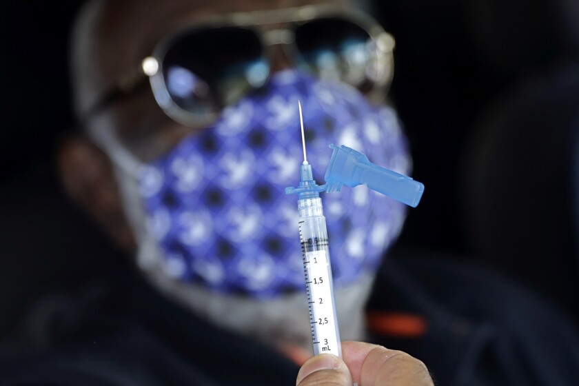 An elderly man looks at the syringe before getting a jab of the Sinovac vaccine at a drive-thru site in Brasilia, Brazil, Thursday, March 11, 2021. (AP Photo/Eraldo Peres)