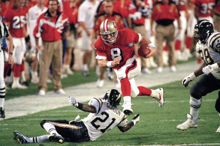 FILE - In this Jan. 29, 1995, file photo, San Francisco 49ers' quarterback Steve Young (8) runs over San Diego's Darrien Gordon (21) for a first down during the first quarter of Super Bowl XXIX at Joe Robbie Stadium in Miami. The NFL became a truly booming business in the 1990s, with multi-billion-dollar TV contracts, expansion to 30 teams, and a late-decade wave of new stadiums. Players began to pick up a bigger share of the wealth, with the dawn of unrestricted free agency. The results on the field were largely dominated by the NFC, with Emmitt Smith and the Dallas Cowboys, Young and the 49ers, and Brett Favre and the Green Bay Packers enjoying the most success. (AP Photo/Andrew Innerarity, File)
