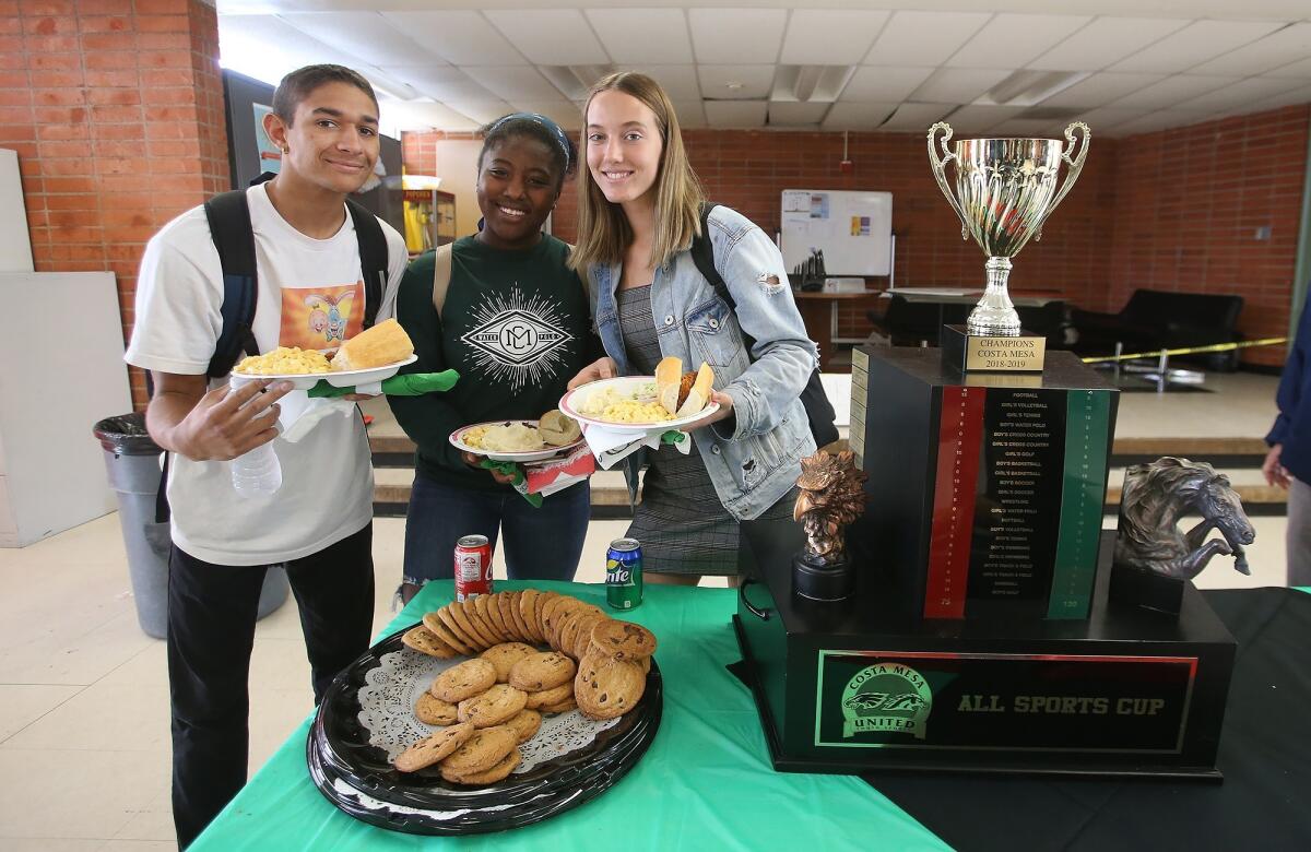 Athletes Tre Villalpando, left, Sey Currie and Angel Carlton stand next to the All-Sports Cup trophy during a celebratory luncheon at Costa Mesa High on Thursday.
