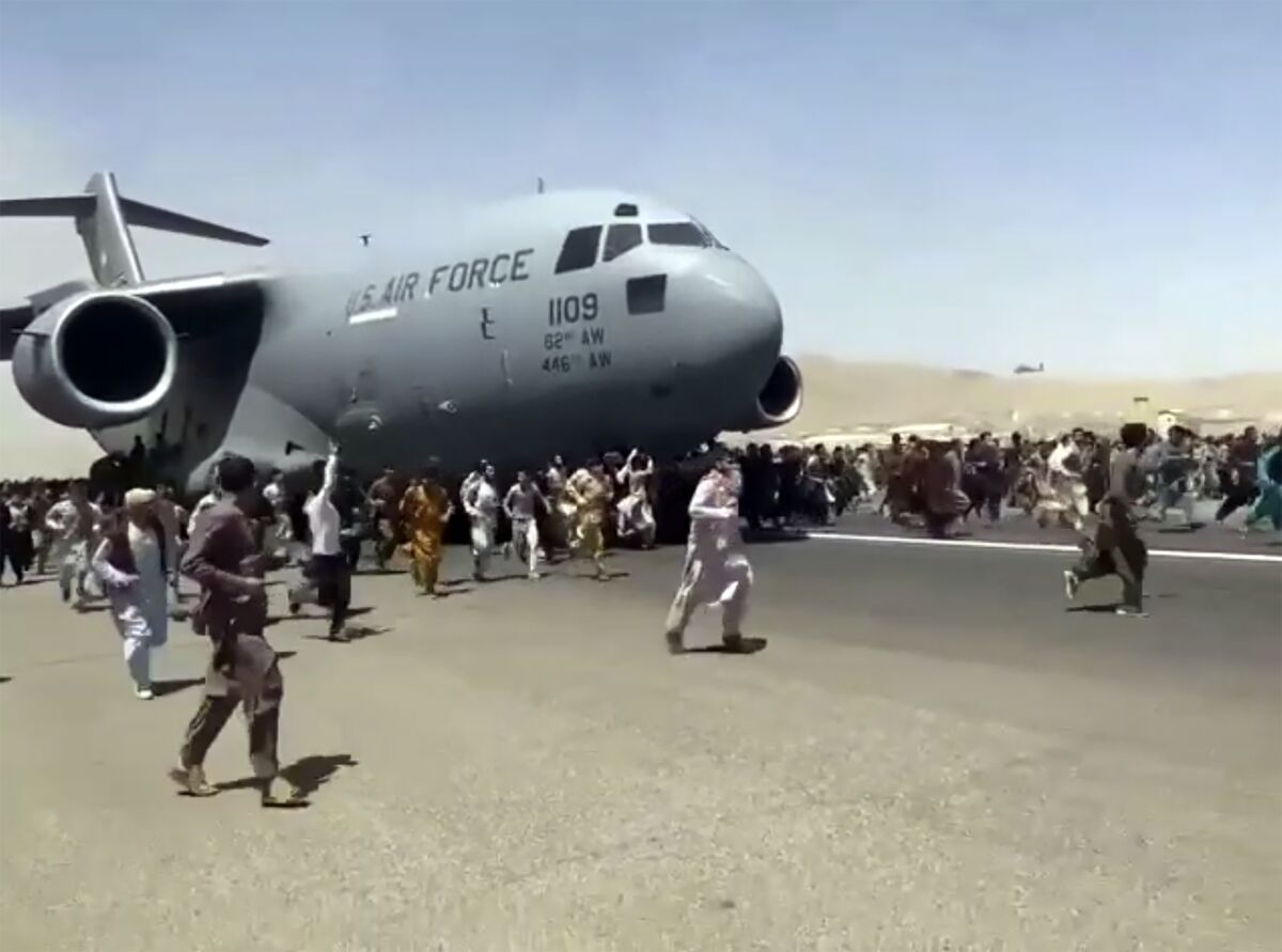 Hundreds of people run alongside a U.S. Air Force C-17 transport plane as it moves down a runway of the Kabul airport.