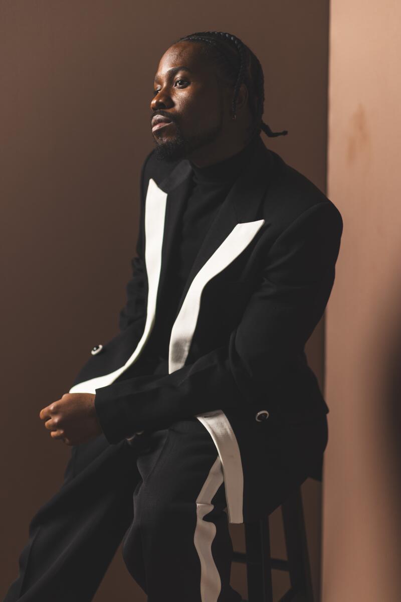 Shameik Moore in a black suit with white trim in a three-quarter view.