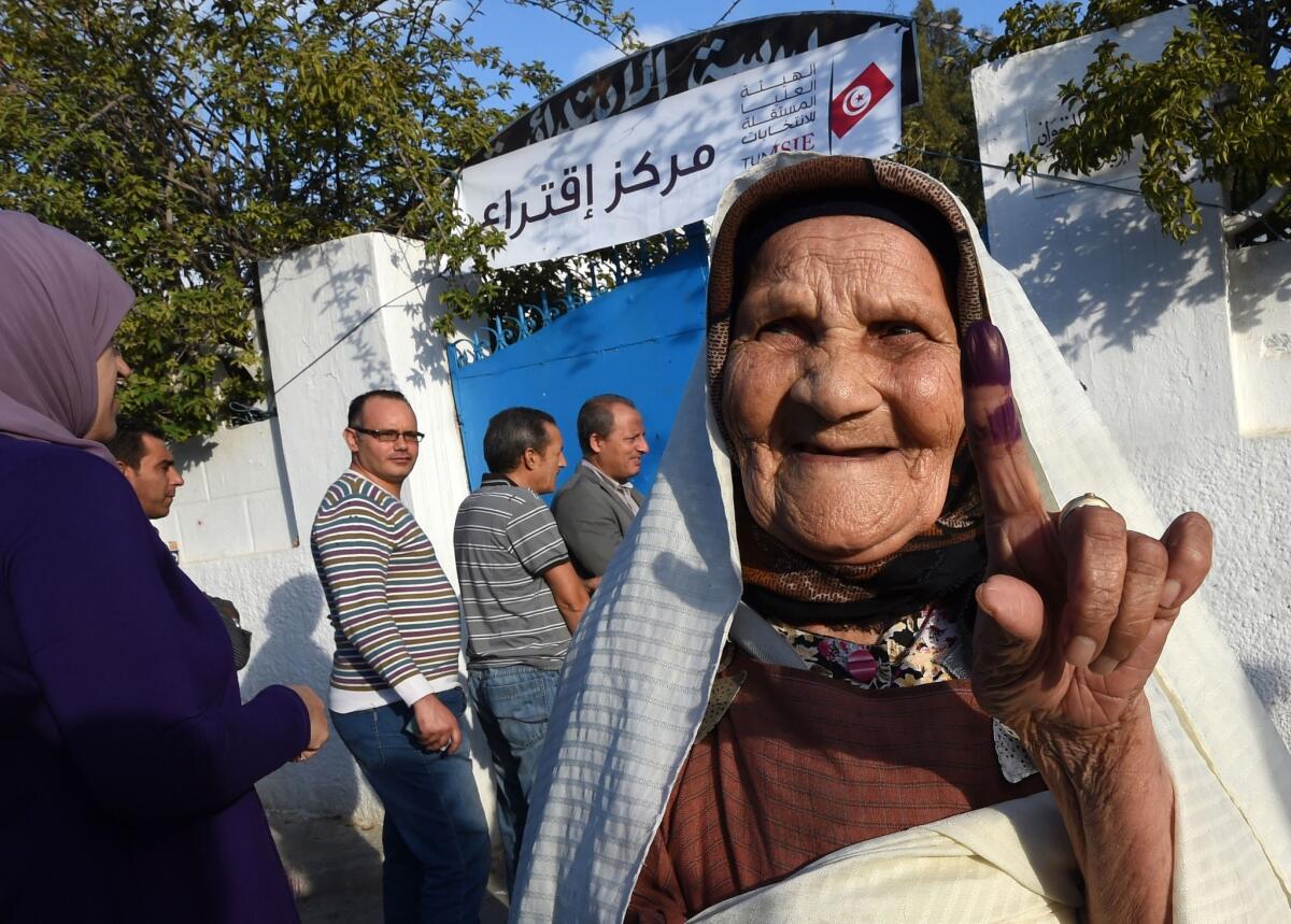 A Tunisian woman shows her ink-stained finger as she leaves a polling station after voting in the country's first post-revolution parliamentary election.