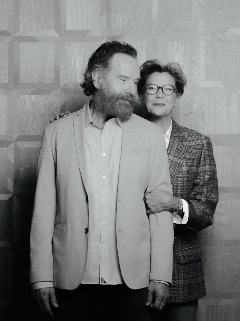 A black-and-white photo of a woman standing behind a man, both wearing blazers.