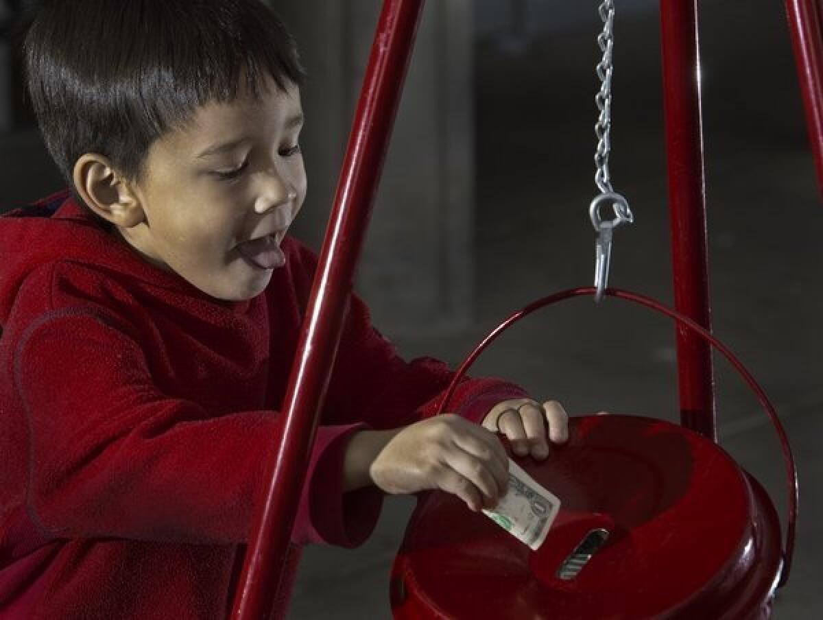 A young boy stuffs a donation into a Salvation Army kettle outside a grocery store in Virginia on Saturday. Unlike the charities that hire commercial fundraising companies, the Salvation Army gets to keep all the money its staff and volunteers collect in its kettles.