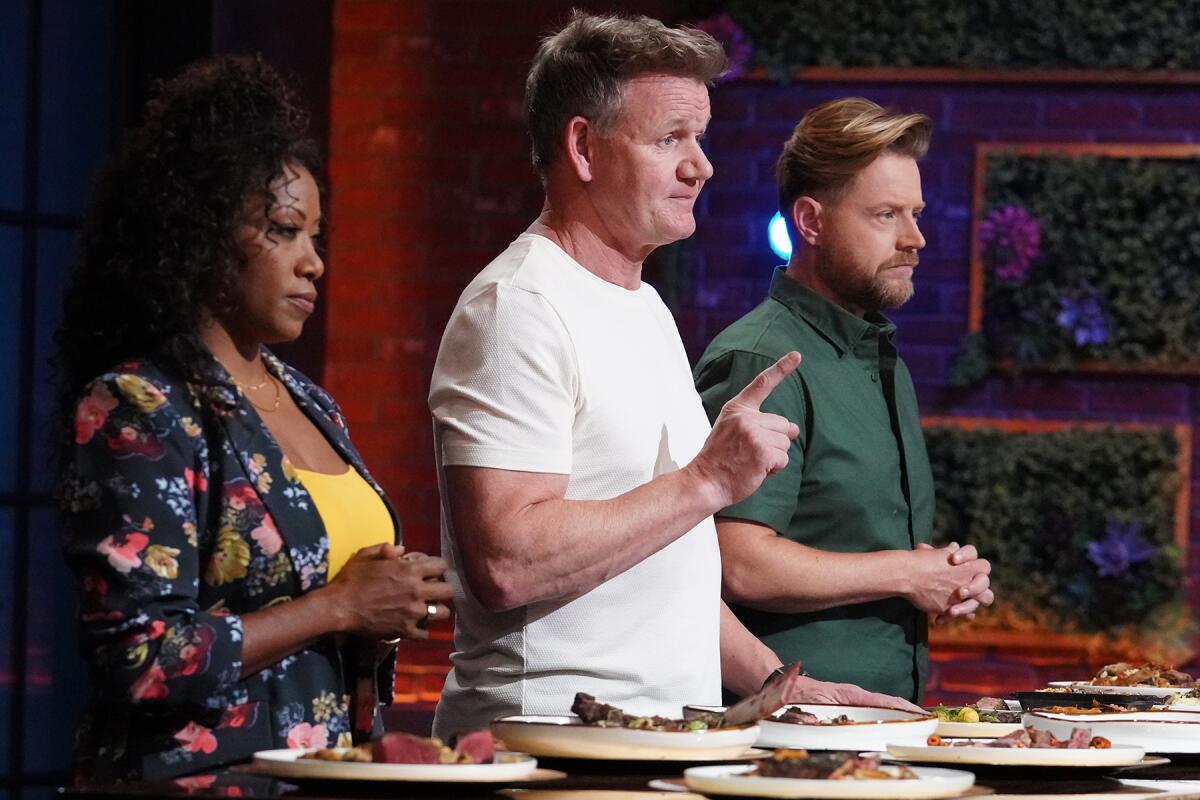 Three people stand behind a table full of prepared dishes