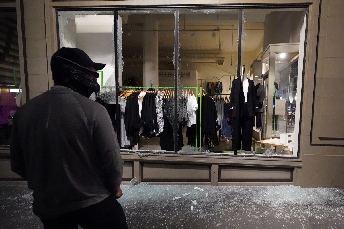 FILE - In this Nov. 4, 2020, file photo, a man stands in front of a broken display window at a retail store during protests in Portland, Ore. Police in Portland say they believe a new state law prohibits officers from directly intervening when people smash storefronts and cause mayhem. The measure passed this year prohibits the use of crowd control methods like pepper spray and rubber bullets "unless use of force is otherwise authorized by statute." (AP Photo/Marcio Jose Sanchez, File)