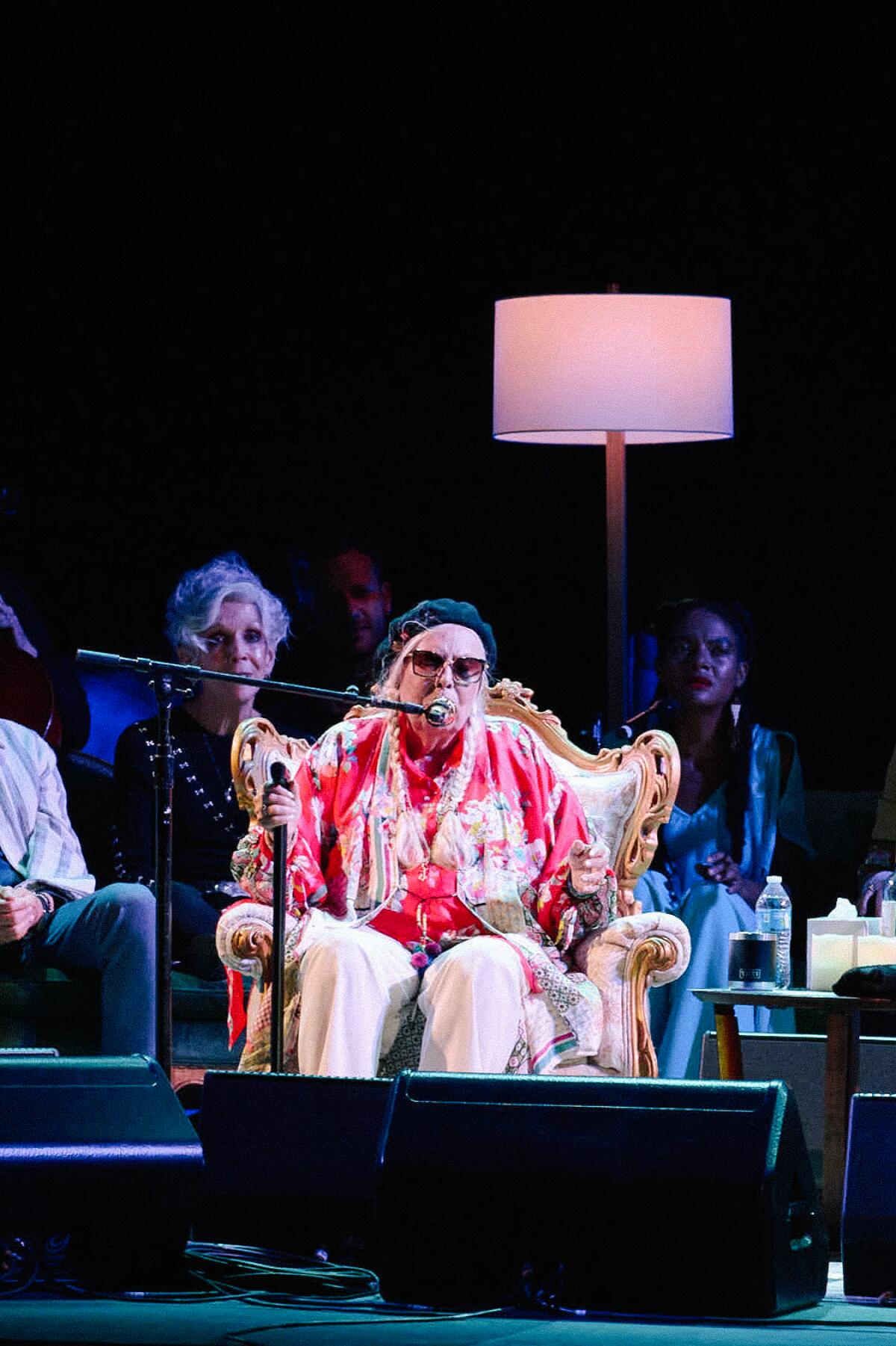 Joni Mitchell sits in an ornate chair on stage.