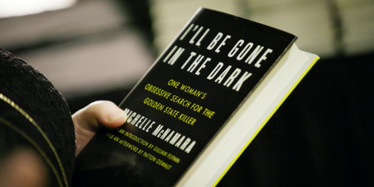 A hand holding a copy of Michelle McNamara's book "I’ll Be Gone In The Dark"