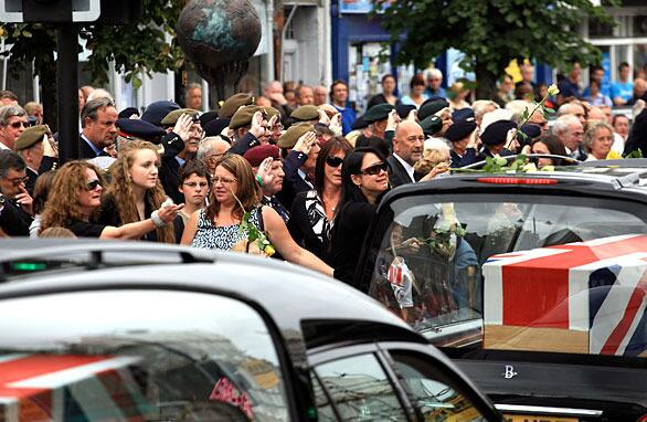 WOOTTON BASSETT, ENGLAND - AUGUST 18: People throw flowers onto the hearses carrying the coffins of Lance Bombardier Matthew Hatton, 23, Rifleman Daniel Wild, 19, and Captain Mark Hale, 42, pass mourners lining the High Street on August 18, 2009 in Wootton Bassett, England. The repatriation to the nearby RAF Lyneham of the bodies of two soldiers and the comrade they died trying to save, is the first since fatalities in Afghanistan passed the 200 mark. Three further soldiers, from 2nd Battalion The Royal Regiment of Fusiliers were killed while on patrol near Sangin on Sunday, bringing the total number of casulties since operations began in 2001 to 204 with the recent rise in numbers largely attributed to Operation Panther's Claw - a surge against the Taliban in central Helman. (Photo by Matt Cardy/Getty Images)