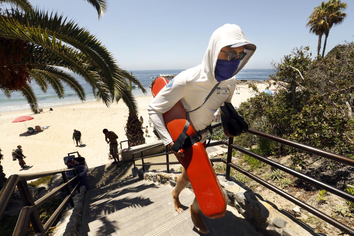 A lifeguard wearing a face covering heads up the steps in Heisler Park in Laguna Beach