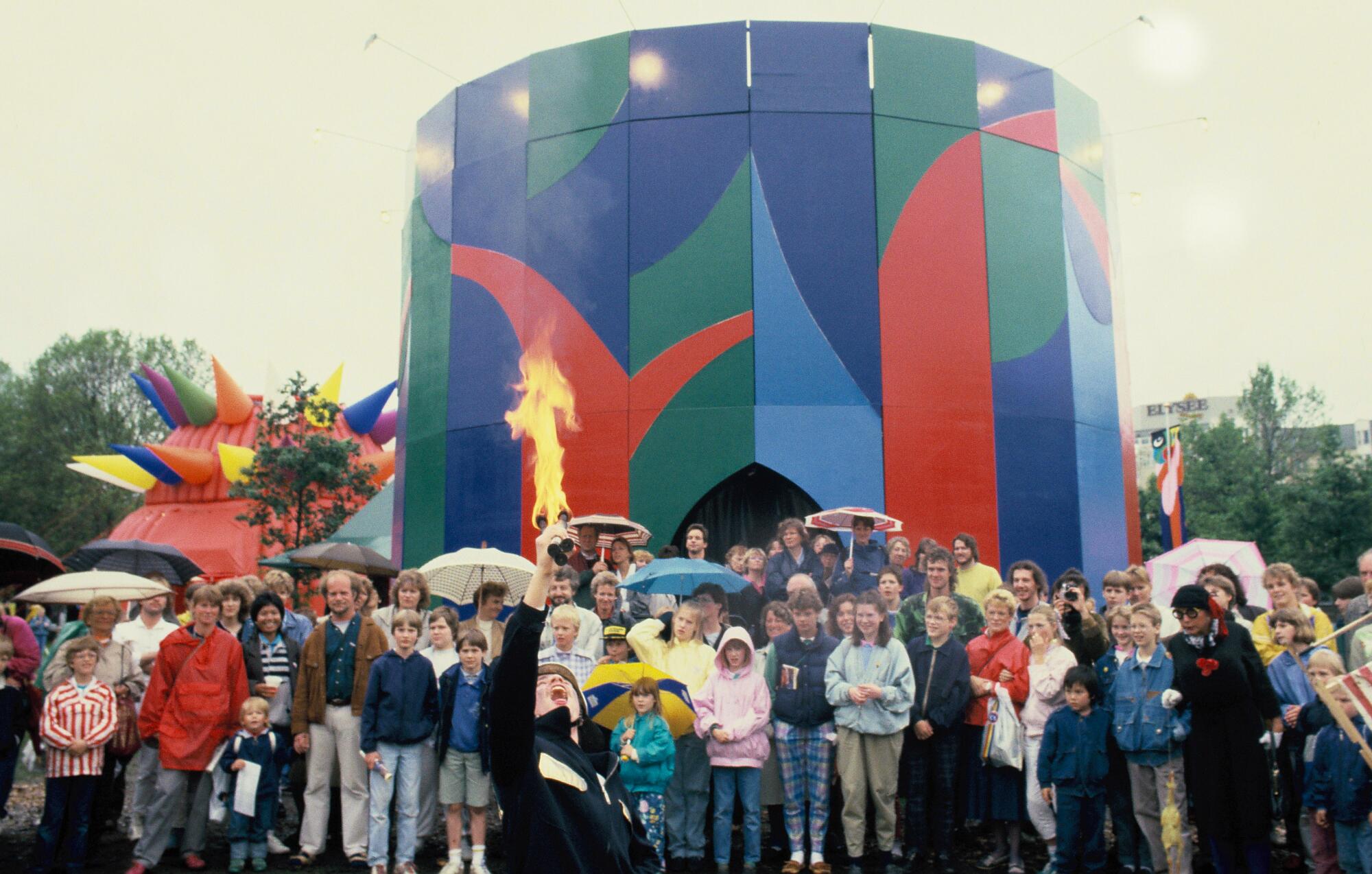 A crowd watches a fire-eating performer outside of a colorfully decorated round structure.