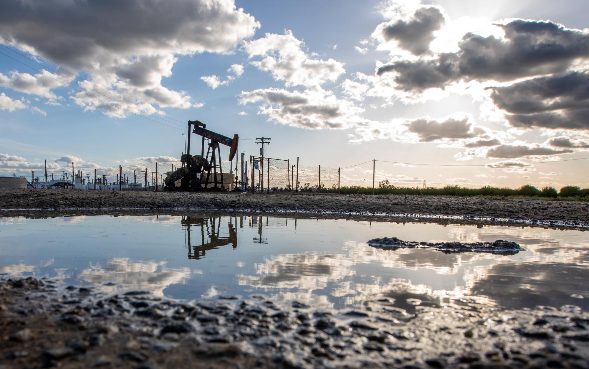 An oil pumpjack is reflected in a puddle of water. 