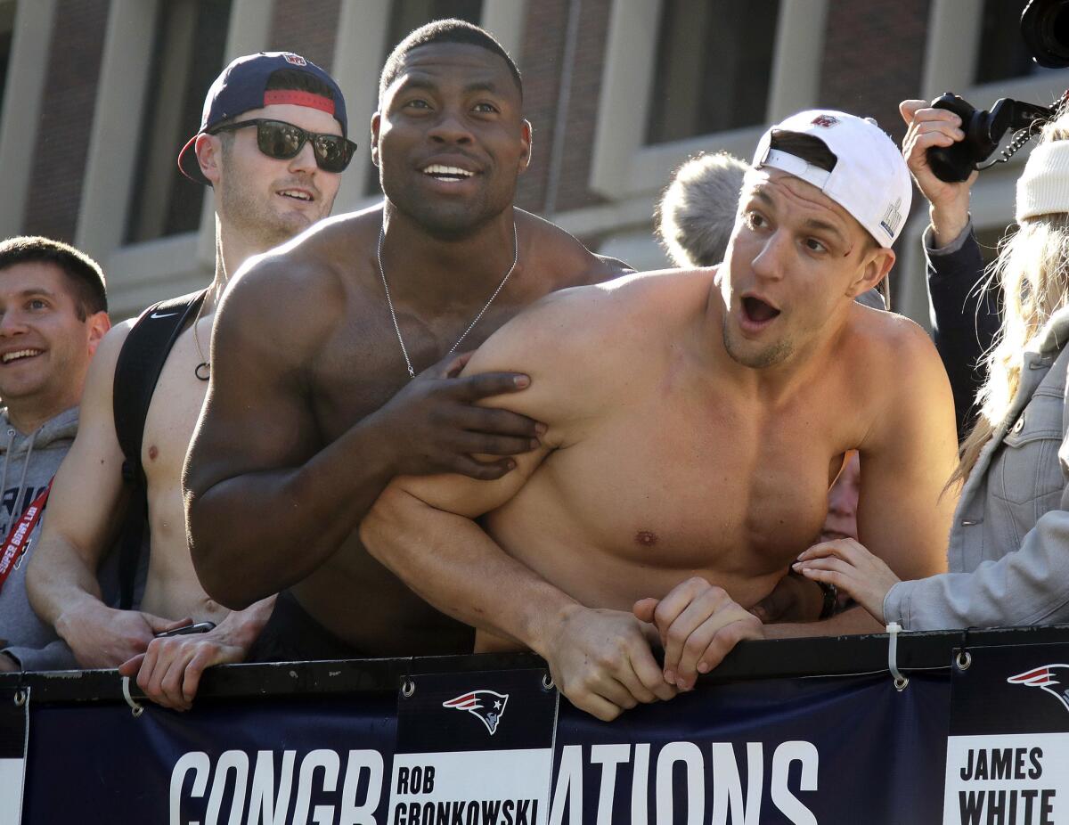 New England Patriots tight ends Dwayne Allen, left, and Rob Gronkowski react to fans during the team's parade through downtown Boston to celebrate their win over the Los Angeles Rams in Sunday's NFL Super Bowl 53 football game in Atlanta. Gronkowski said he was hit in the face by a can of beer thrown during the parade, causing a small cut near his left eye.