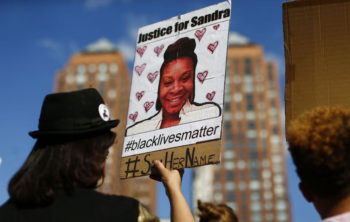 A woman holds a poster bearing the portrait of Sandra Bland.