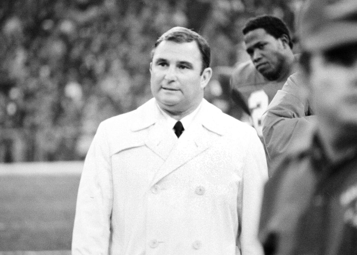 A man in a coat and tie watches from the sideline.