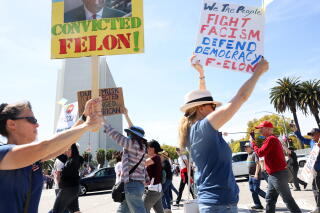 Several people outdoors hold signs against President Trump and fascism.