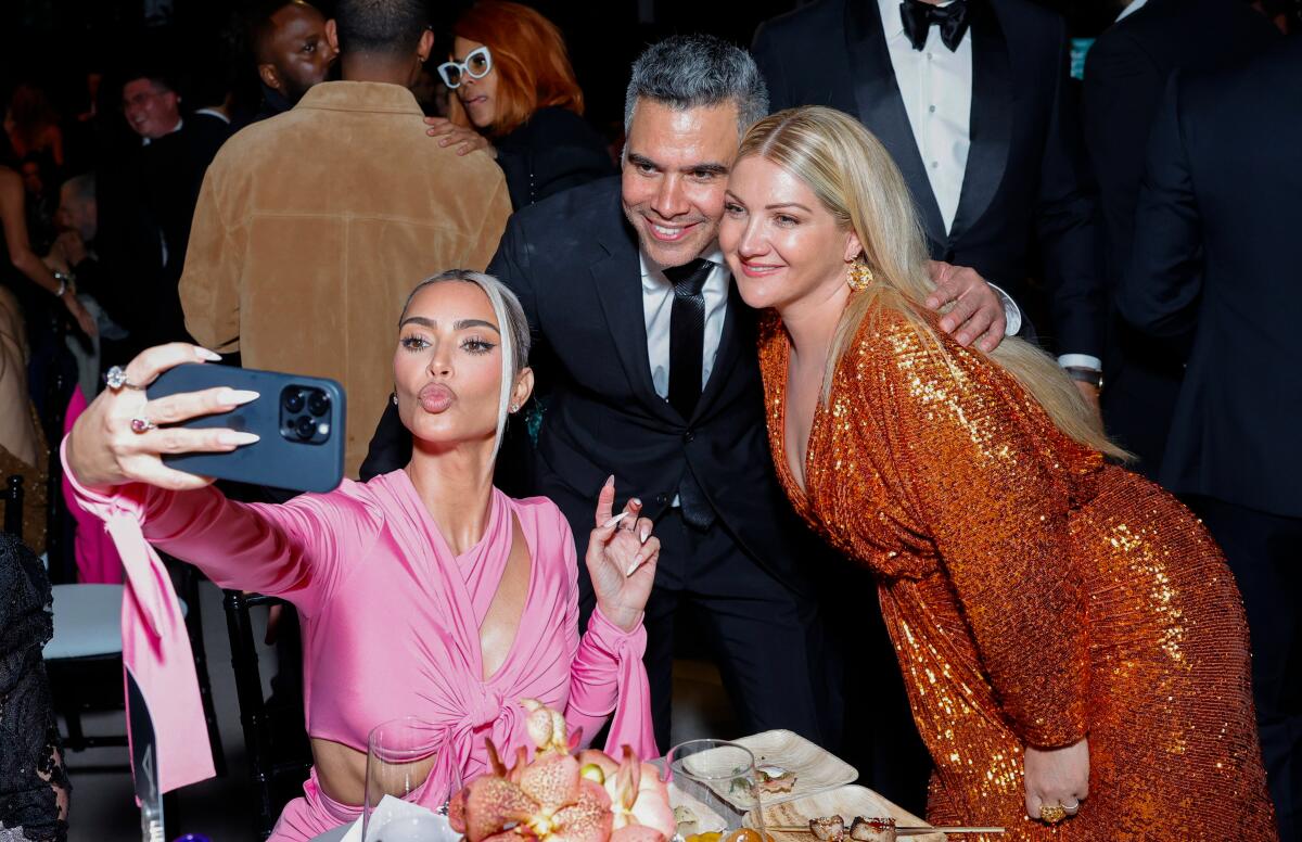 A woman makes fish lips while taking a selfie with a man and woman. All are in formal wear.