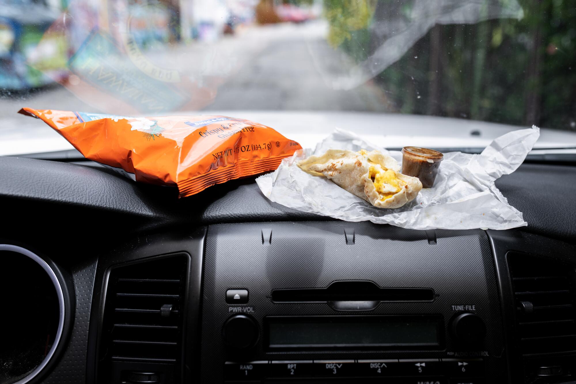 A taco and a bag of chips atop a black dashboard.
