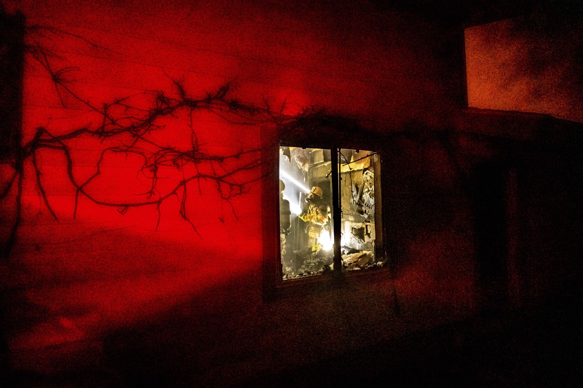 A firefighter illuminated in light inside a home, seen through the window