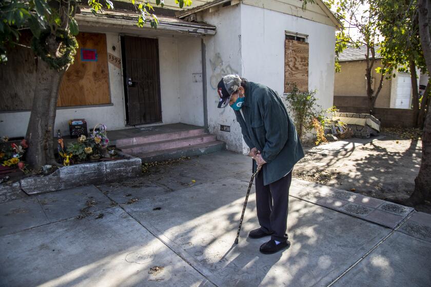 SAN BERNARDINO, CA - DECEMBER 17, 2020: Juan Gutierrez looks down at the writings in the cement of his children names in the front yard of a house he bought in 1968 and lived in for 50 years until reverse mortgage lenders foreclosed on him and he was evicted on December 17, 2020 in San Bernardino, California. He worked in construction and saved enough money to buy the house in 1968, but he suffered a crippling injury in a job-site accident and lived on disability for years. After his wife died and the kids moved out, the house fell into disrepair so he took out a reverse mortgage to stay in the home, but it was the beginning of a nightmare now 6 years running.(Gina Ferazzi / Los Angeles Times)