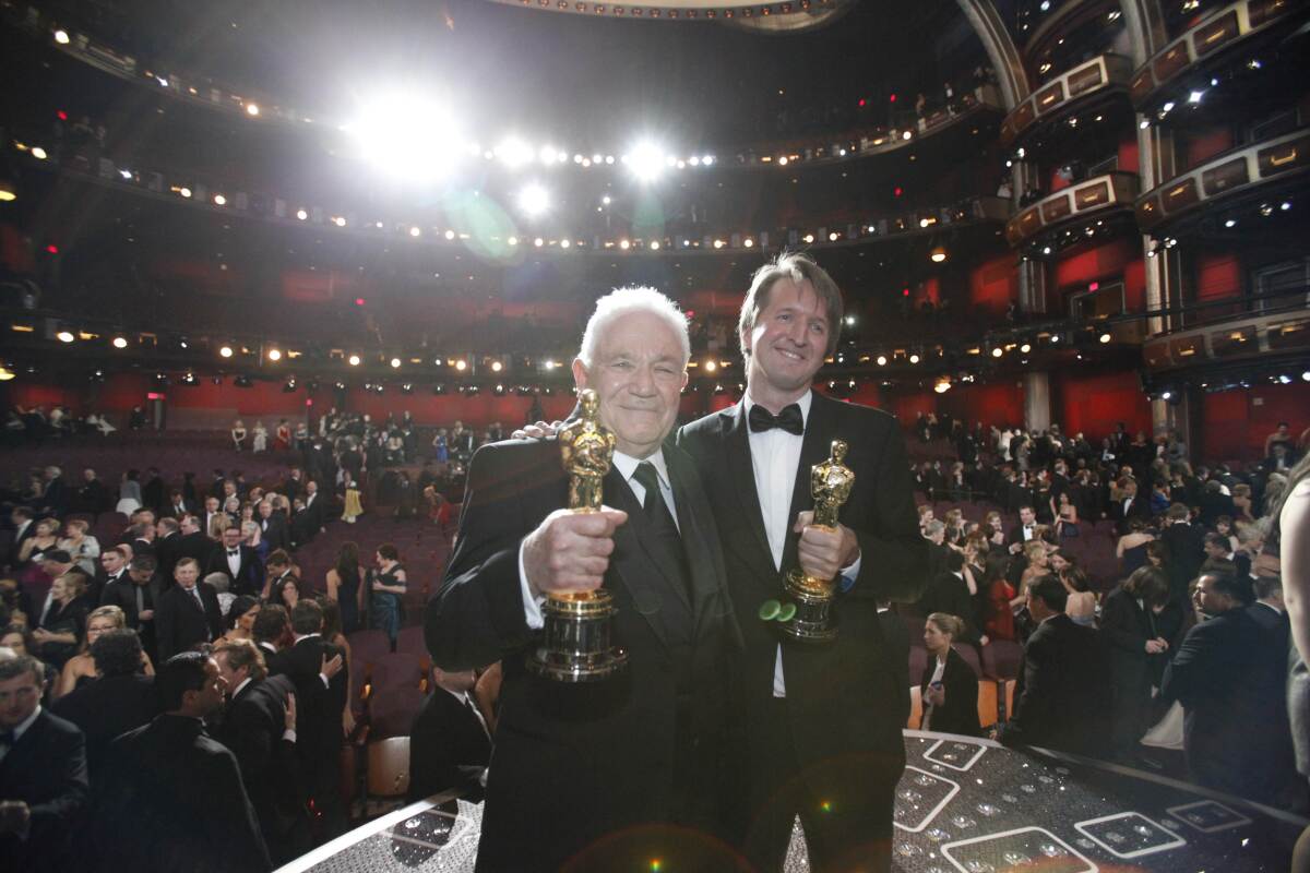 Two men in tuxes show off their Oscars during an awards show.