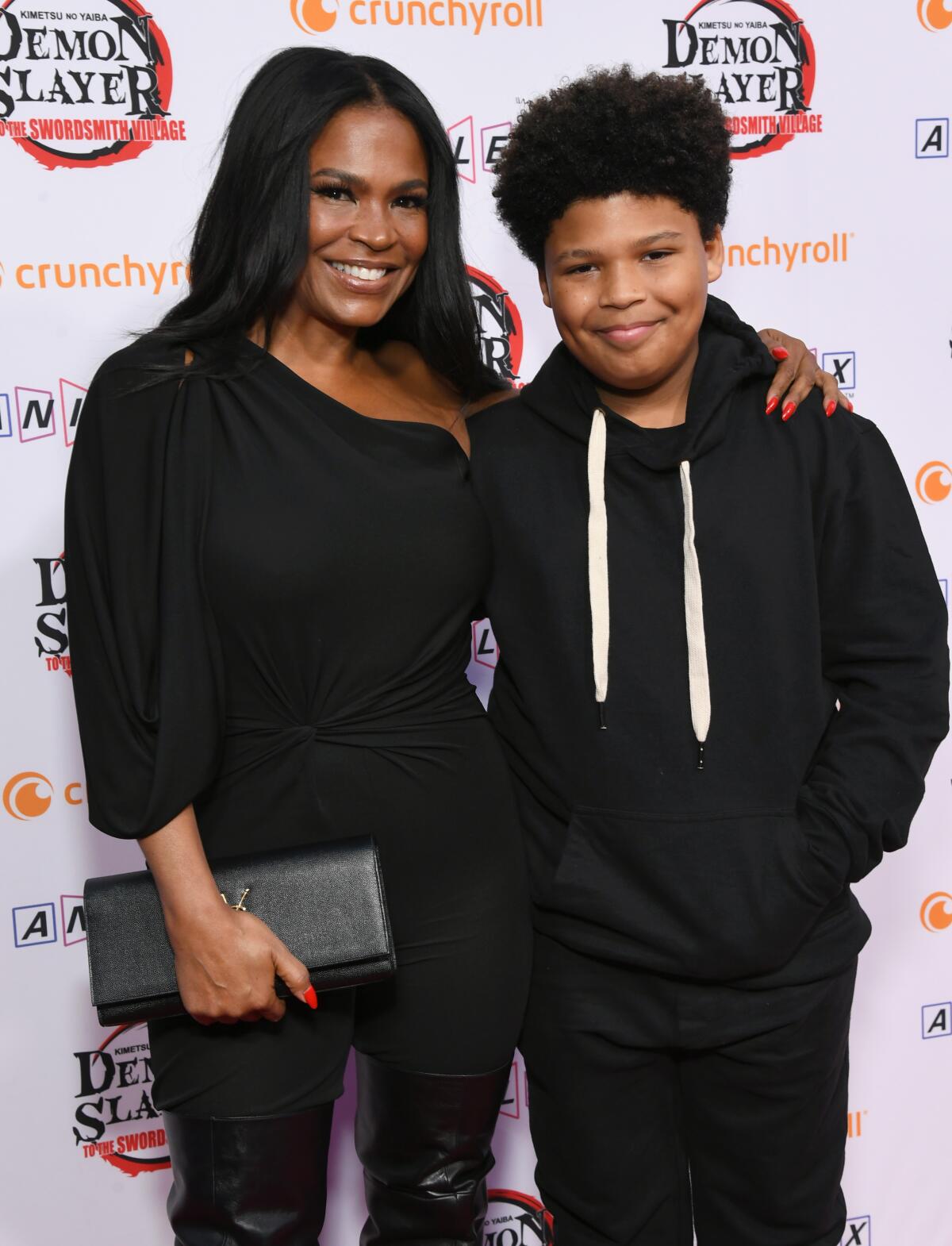 A woman with black hair poses with her son. They are wearing all black.