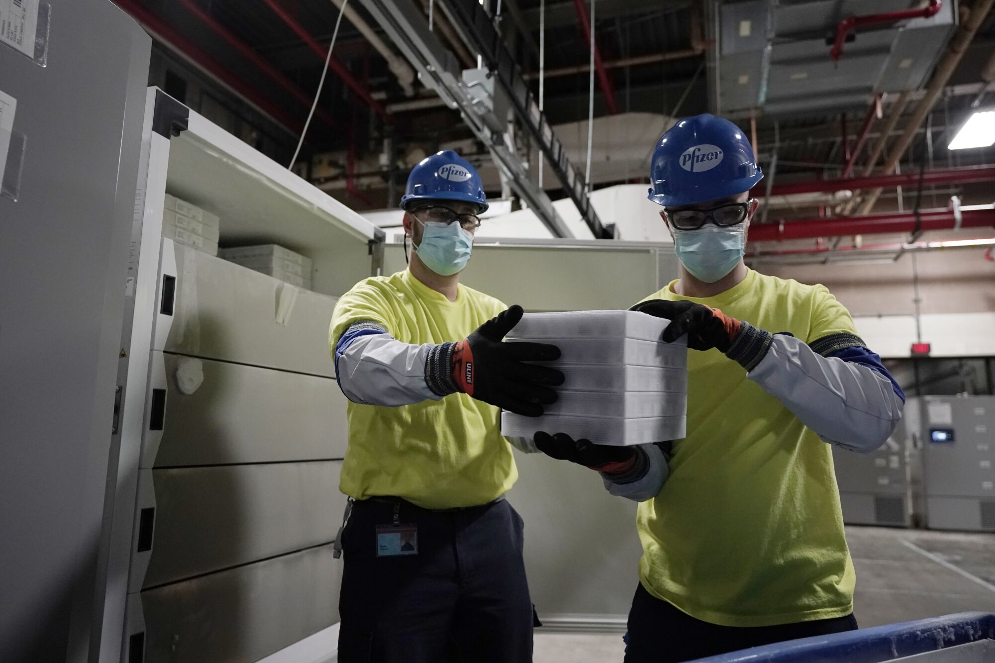 Two workers hold boxes of vaccine at a manufacturing plant.
