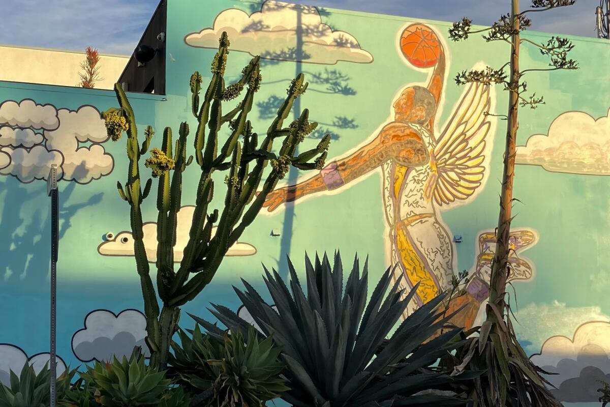 Kobe Bryant is flying through the air with wings and palming a basketball in a mural outside Planet Salon.