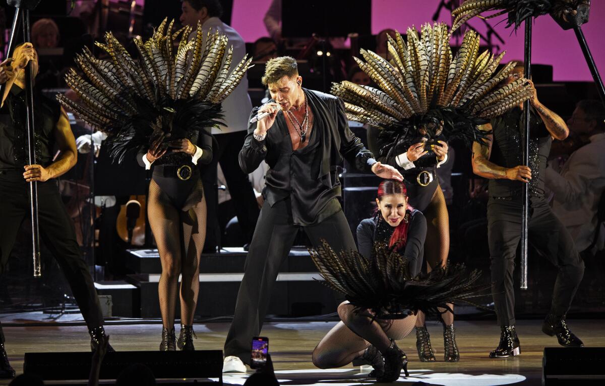 A male singer, dressed in black, and his backup dancers, onstage.