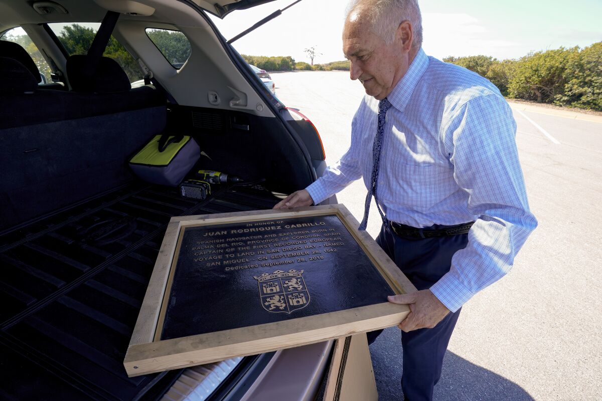 A man holds a plaque at the back of a vehicle