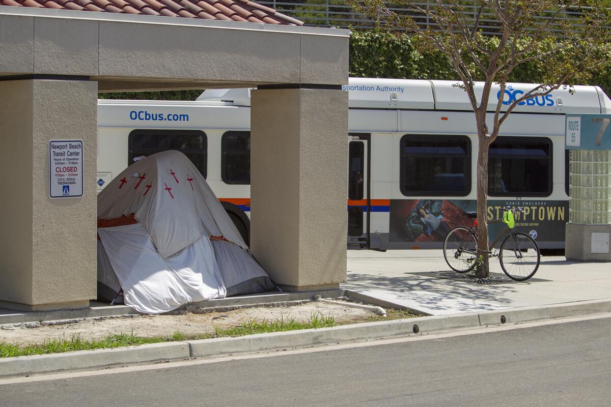 A tent is set up under a shade structure at the Newport Beach bus station on Avocado Avenue. OCTA has given Newport police the go-ahead to enforce against trespassing when buses aren't running.