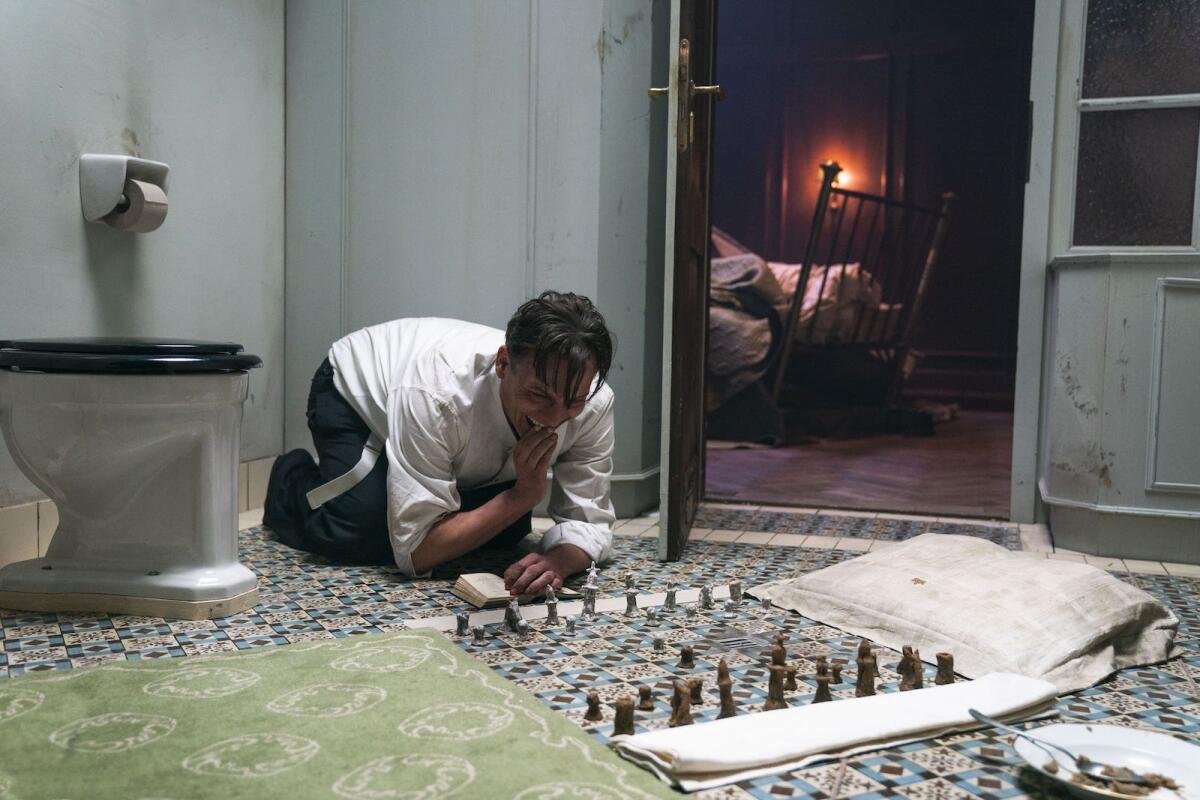 A man on a bathroom floor studies chess pieces in the movie "Chess Story."