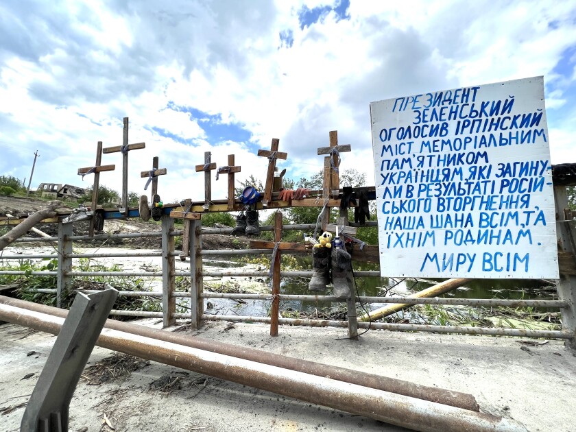 Crosses atop a bridge railing near a white sign with blue lettering in Ukrainian 