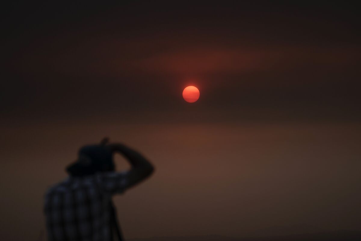 Jason Anderson, 42, takes pictures as the sun is visible through thick smoke generated by the Bobcat Fire in San Dimas, Calif., Wednesday, Sept. 9, 2020. Hazy clouds of smoke from dozens of wildfires darkened the sky to an eerie orange glow over much of the West Coast on Wednesday, keeping street lights illuminated during the day and putting residents on edge. (AP Photo/Jae C. Hong)