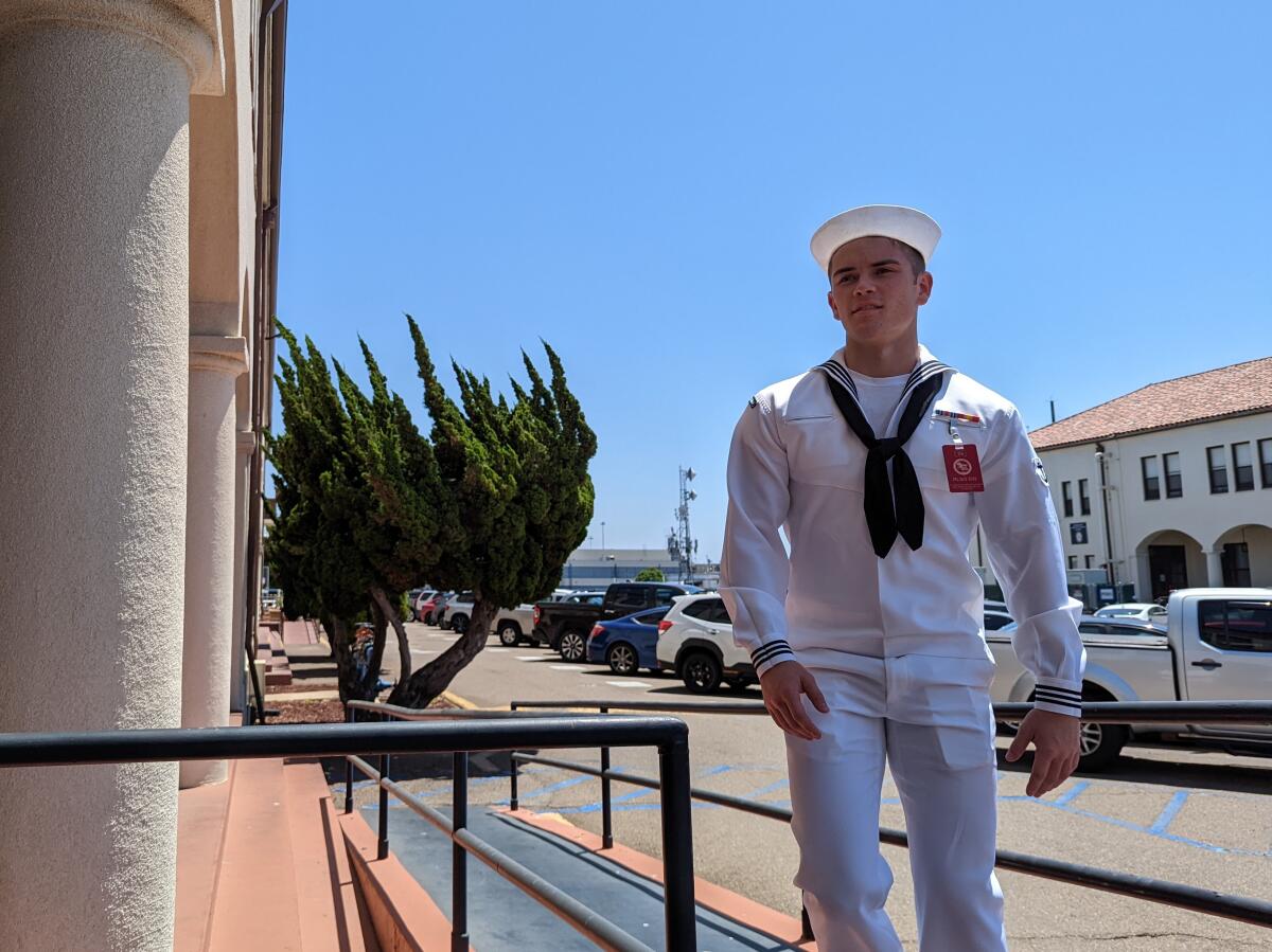A man in a Navy sailor uniform walks up a ramp outside a building.