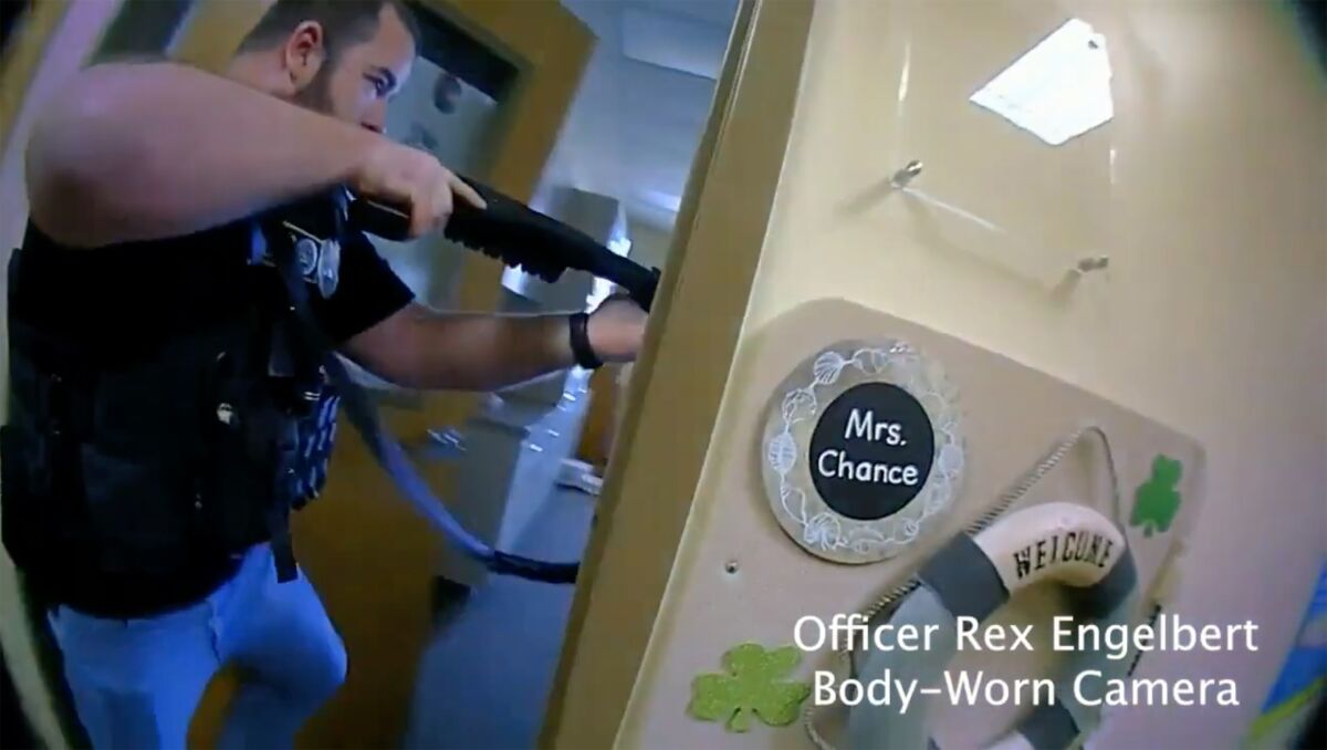An armed police officer holds a gun in a school hallway in an image from video.