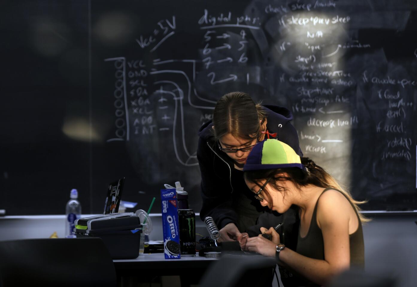 The morning sun hits Elizabeth Poss, 19, left, and Lauren Hu, 20, as they work on their "Sleep Dep Buddy" project at the MuddHacks, a Harvey Mudd College hardware hackathon, in October. The light-sensitive robot was designed to cause a ruckus if its owner doesn't turn off the light and go to bed to get enough sleep.