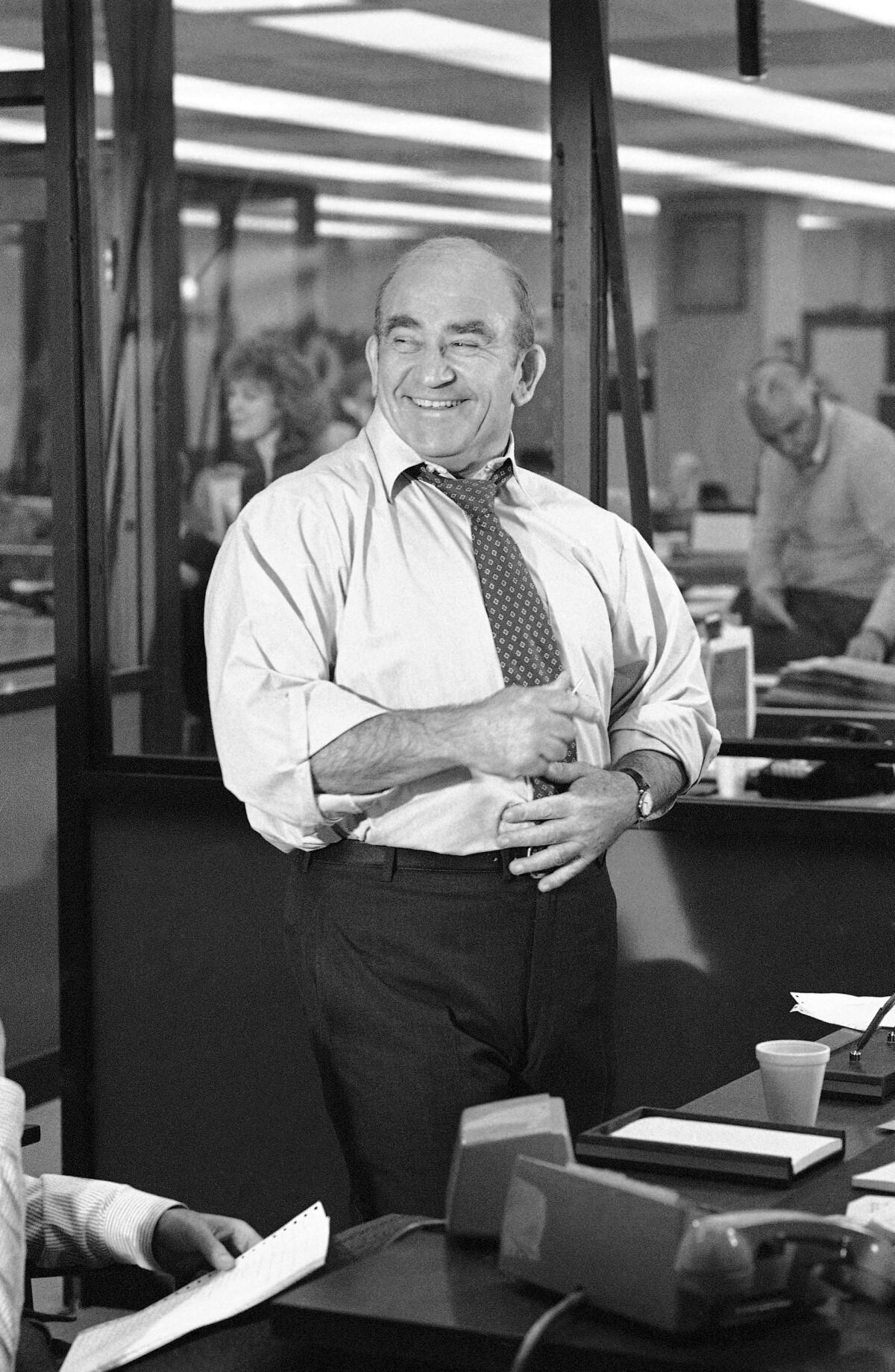 A man in a tie stands in a newsroom office