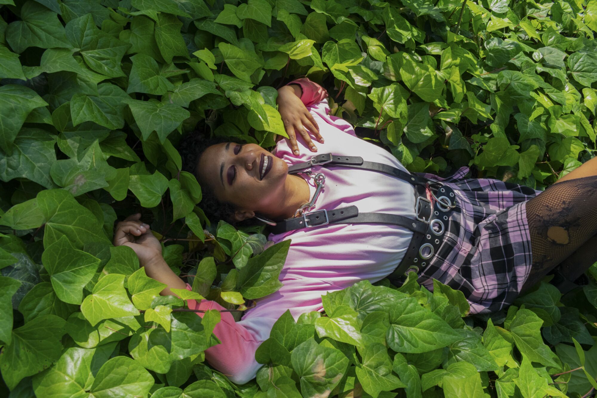A photograph of a woman lying in a bed of groundcover plants