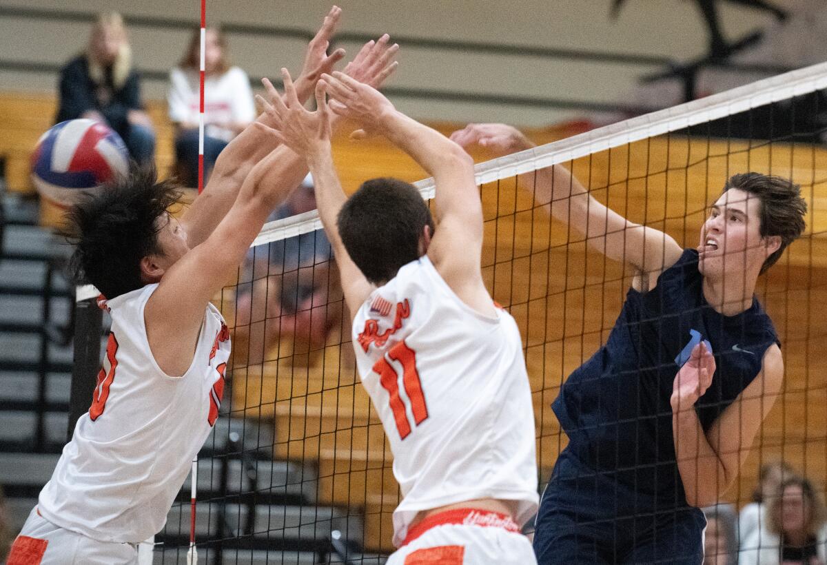 Corona del Mar's Sterling Foley hits off the block of Huntington Beach's Colin Choi, left, and Logan Hutnick (11) on Tuesday.